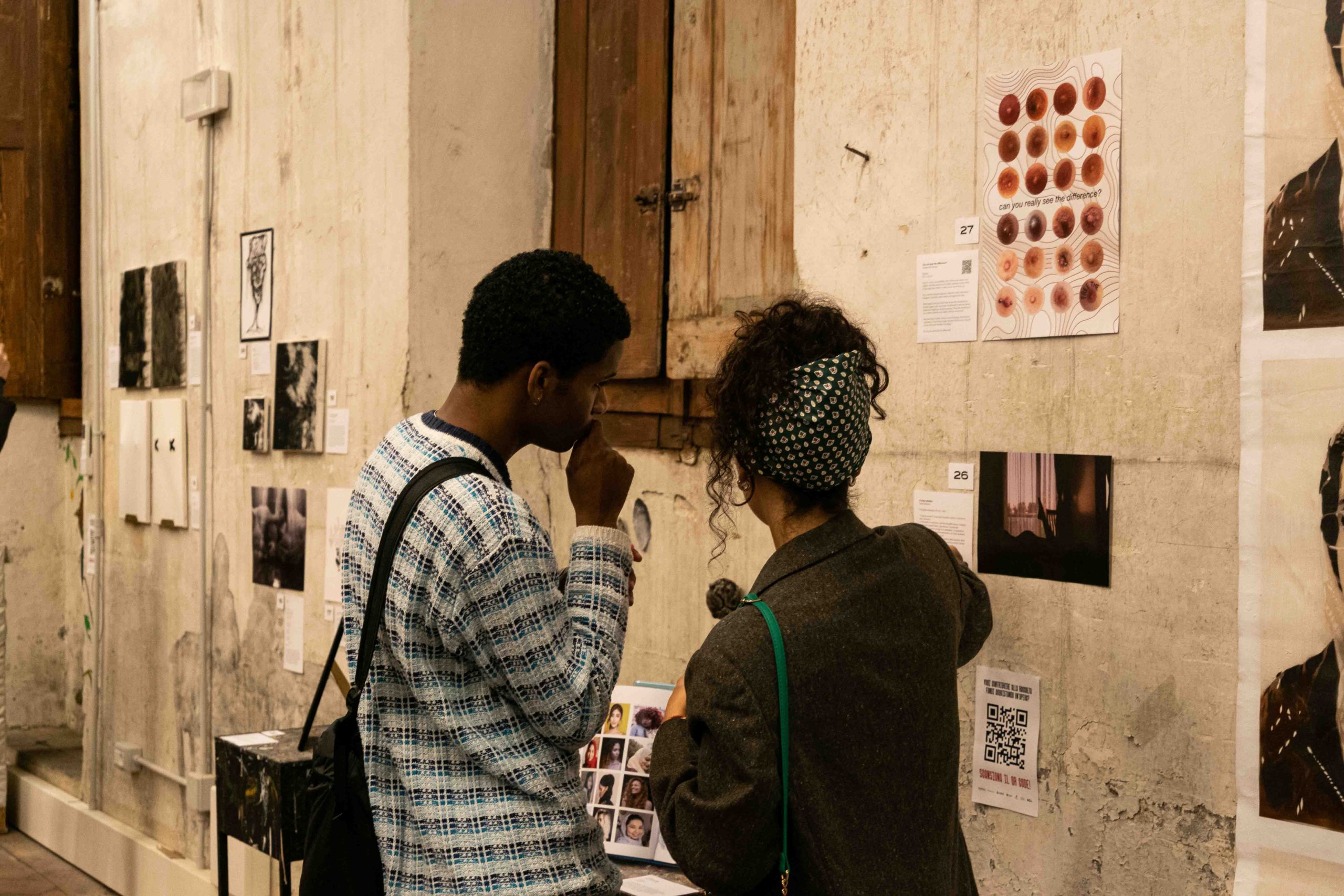 Due persone osservano opere d'arte esposte su un muro in una galleria, scambiando opinioni.