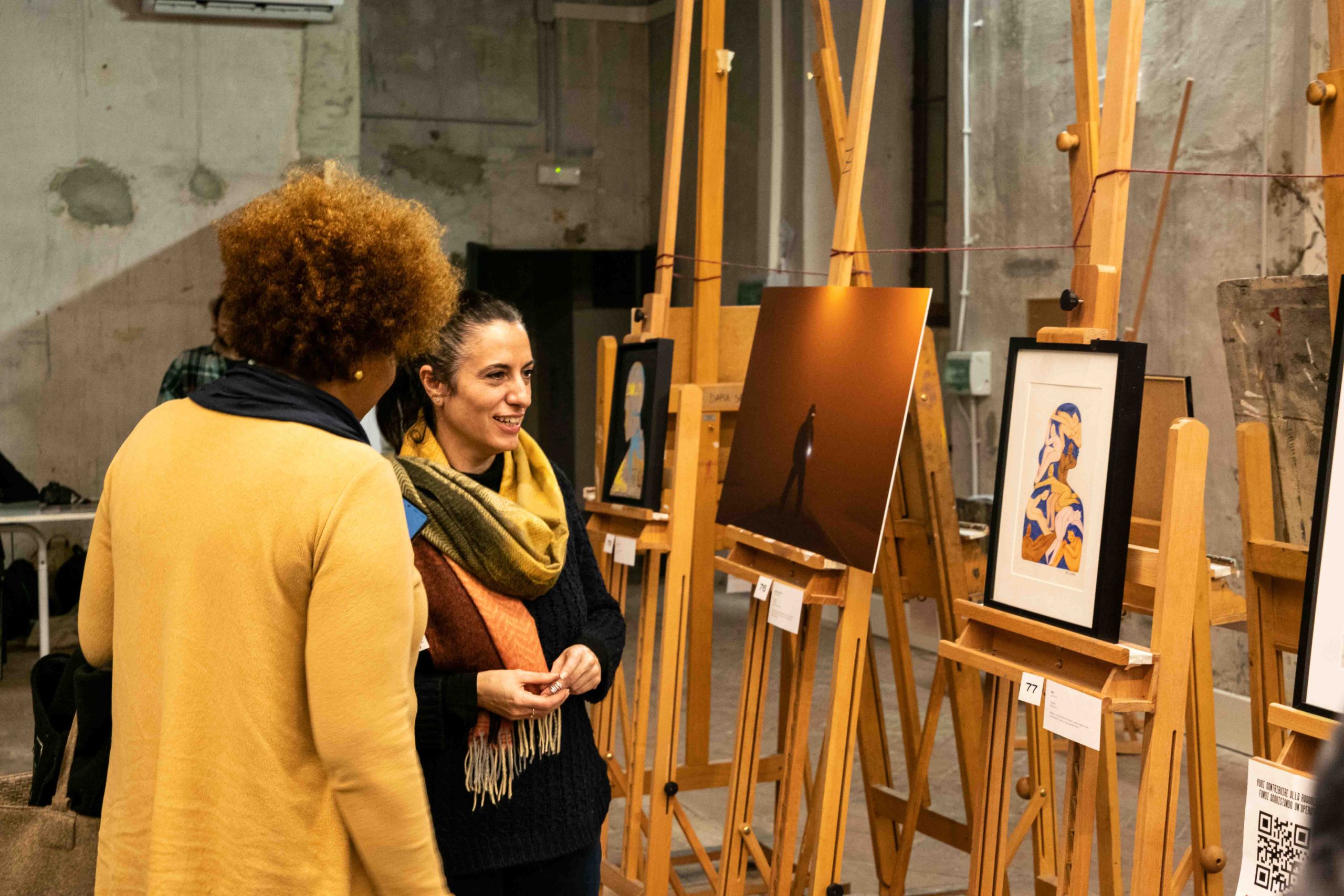 Due persone discutono di opere d'arte in una galleria, circondate da quadri su cavalletti di legno.