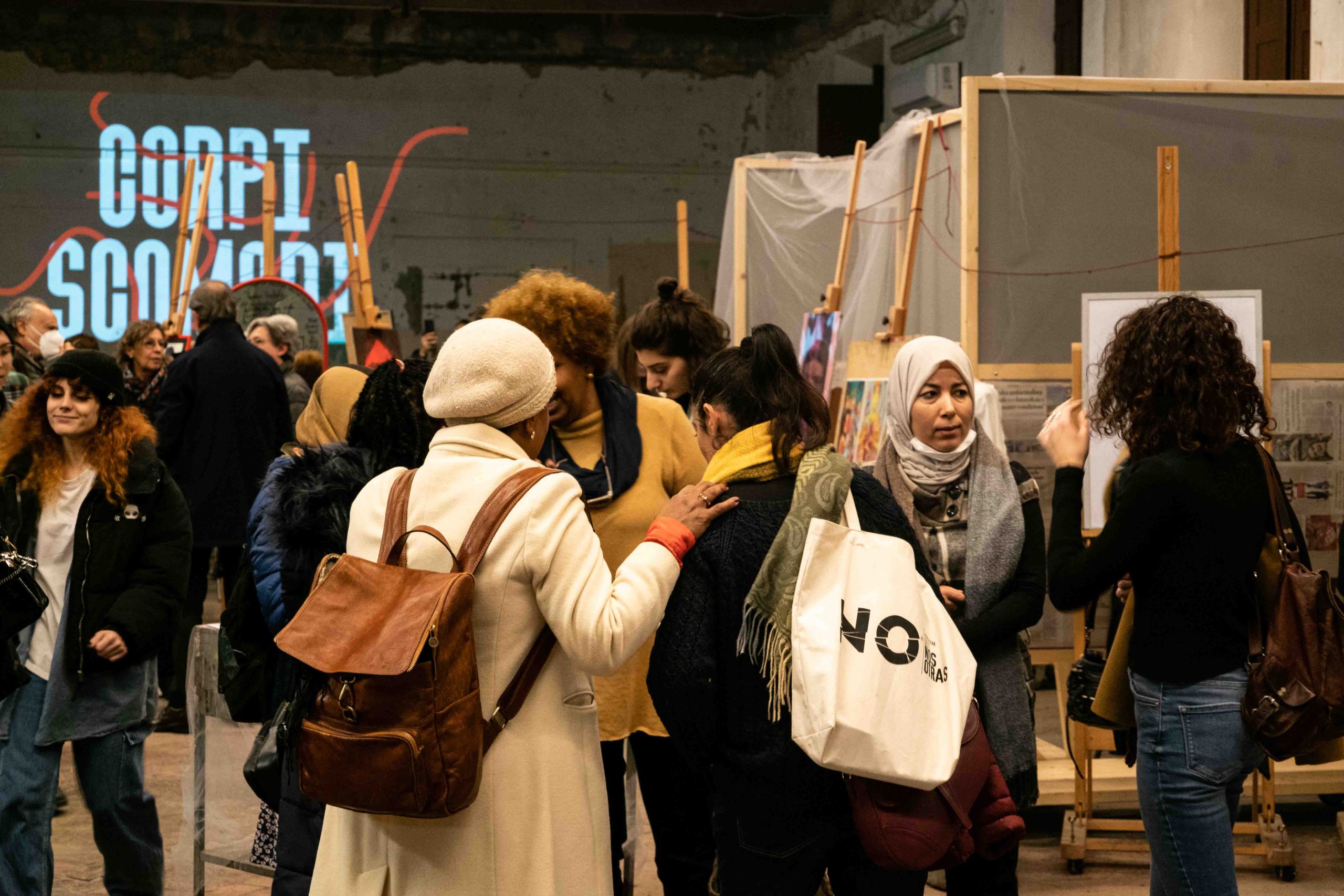 Gruppo di persone interagisce all'interno di una mostra d'arte con pannelli espositivi sullo sfondo.