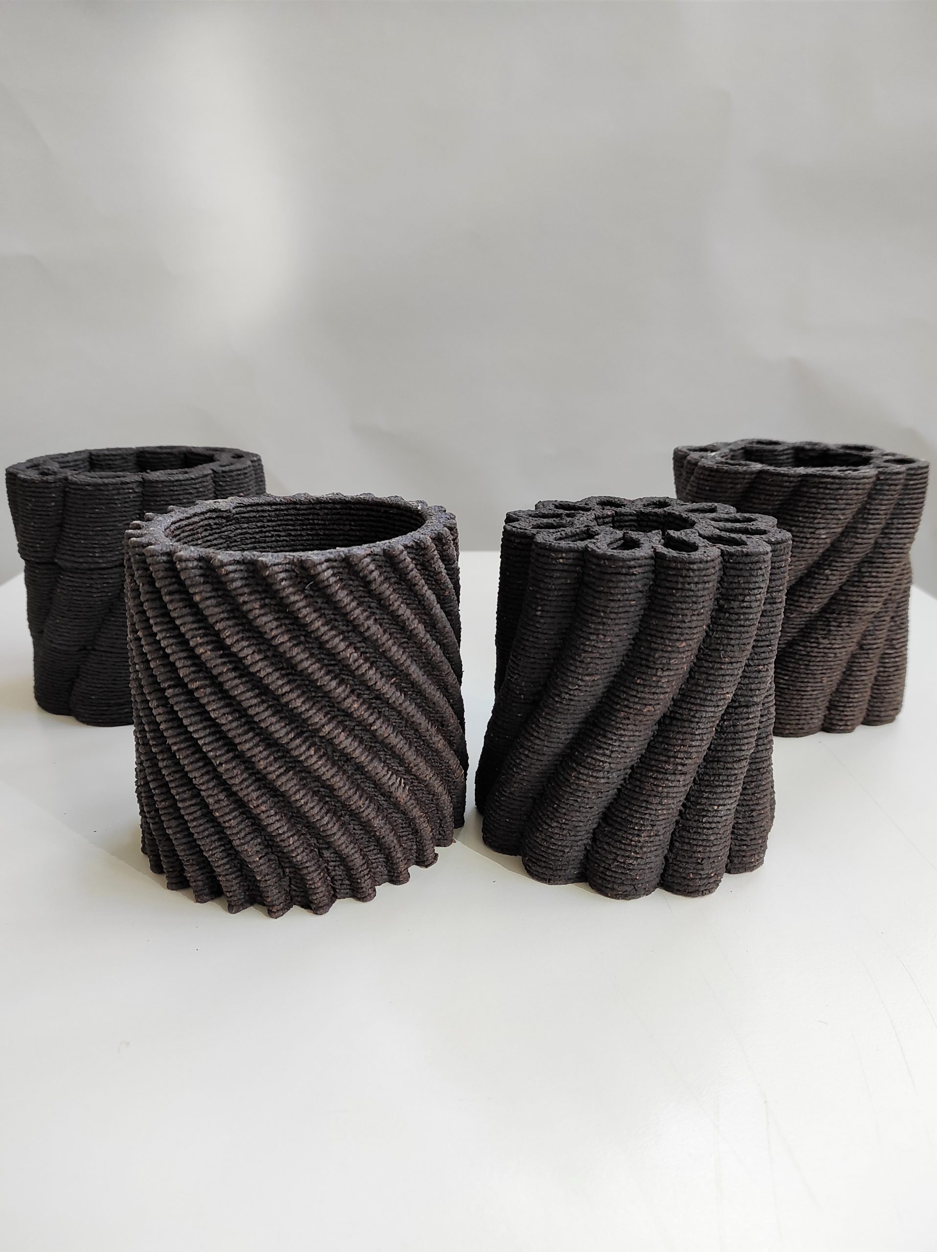 Quattro vasi neri in ceramica 3D con design a spirale su sfondo neutro.