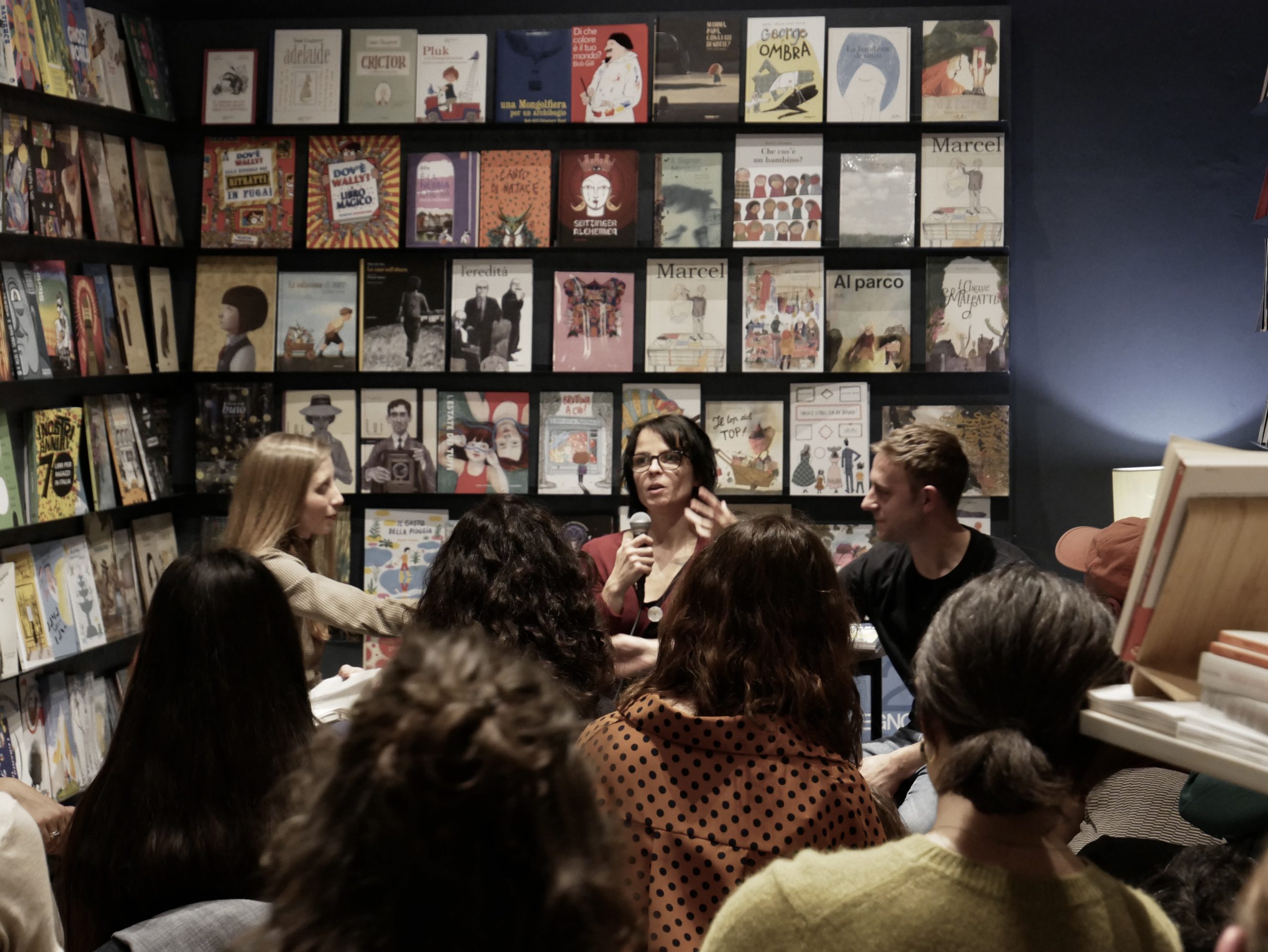 Gruppo di persone discute in una libreria, con scaffali pieni di libri colorati sullo sfondo.