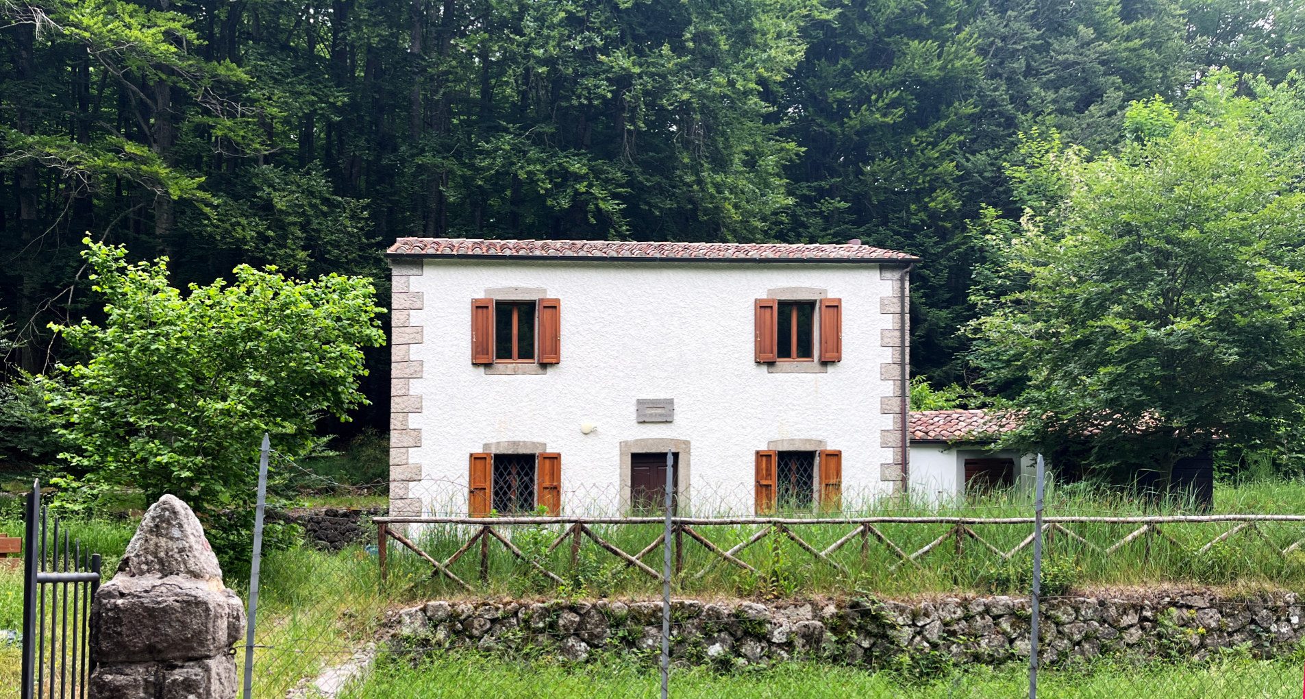 Casa rurale bianca con persiane in legno, immersa nel verde di una foresta lussureggiante.