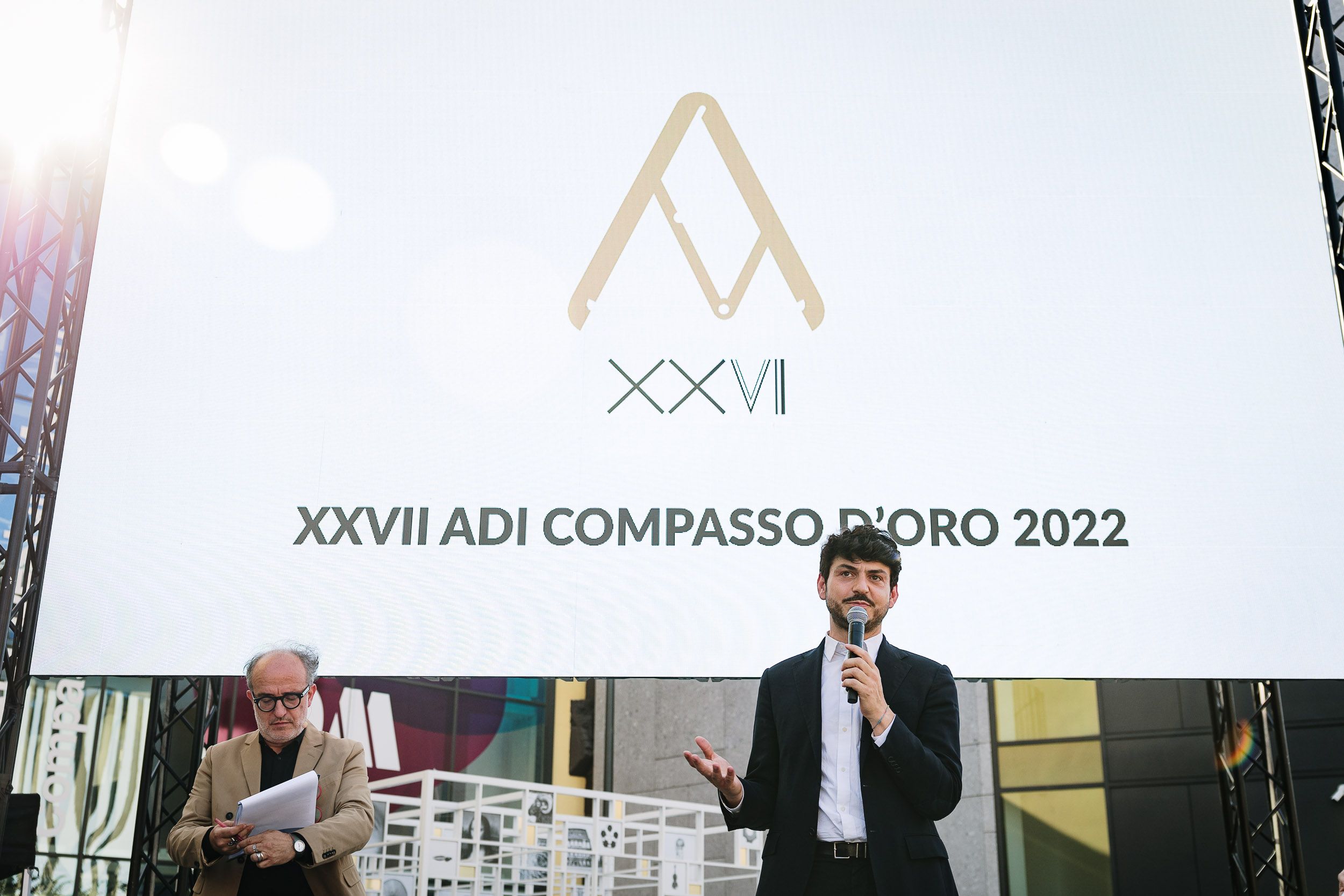 Presentazione del XXVII Compasso d'Oro ADI 2022, uomo con microfono e logo sullo schermo.