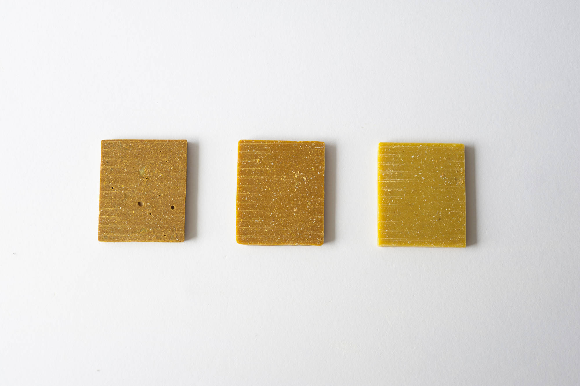 Tre quadrati giallo-marroni su sfondo bianco, texturizzati e posizionati in fila.