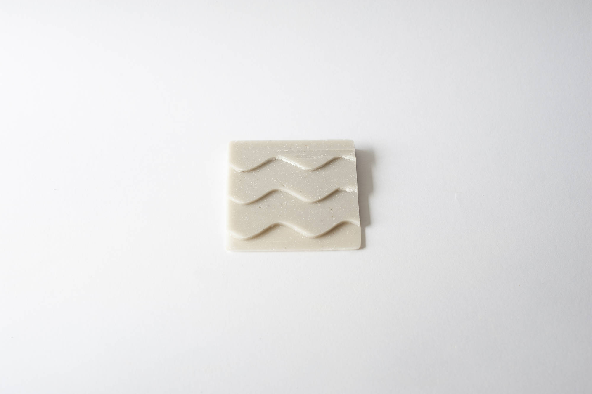 Piastrella quadrata in ceramica bianca con motivo a onde su sfondo bianco.