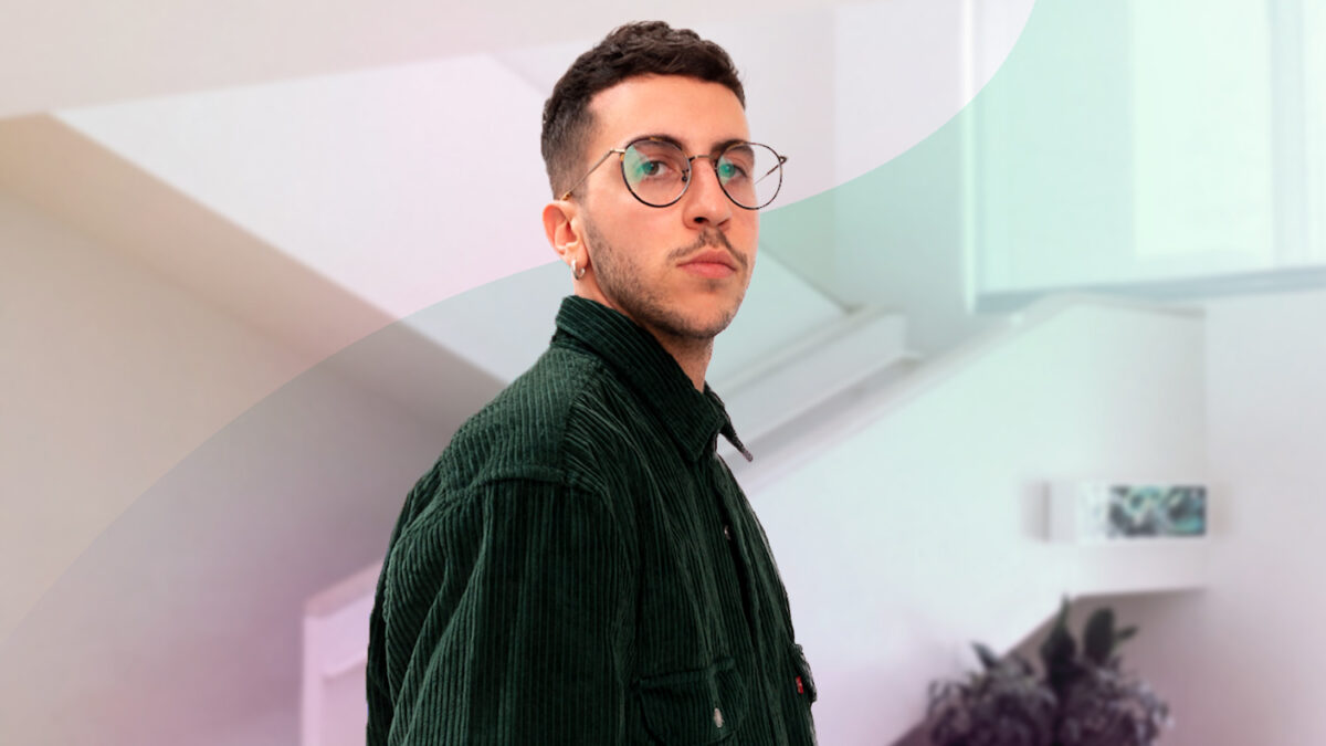 Giovane uomo con occhiali e giacca verde, in piedi in un ambiente moderno e luminoso.