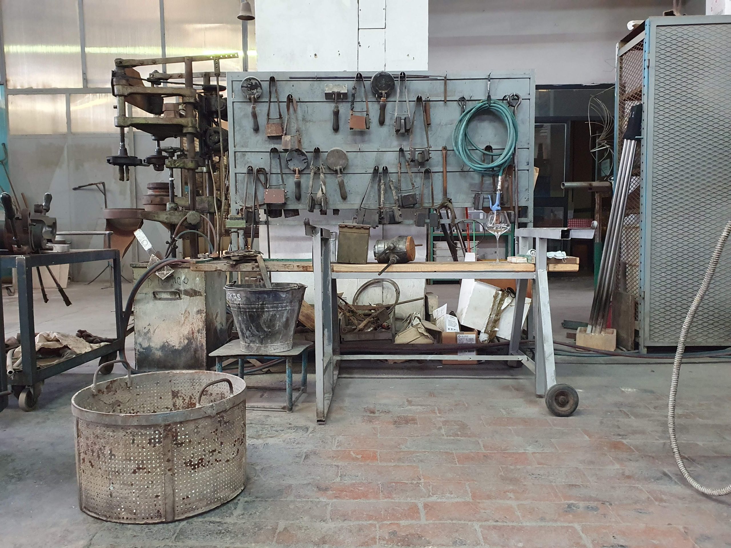 Officina tradizionale con attrezzi appesi e macchinari, evidenziati strumenti per lavori artigianali e meccanici.