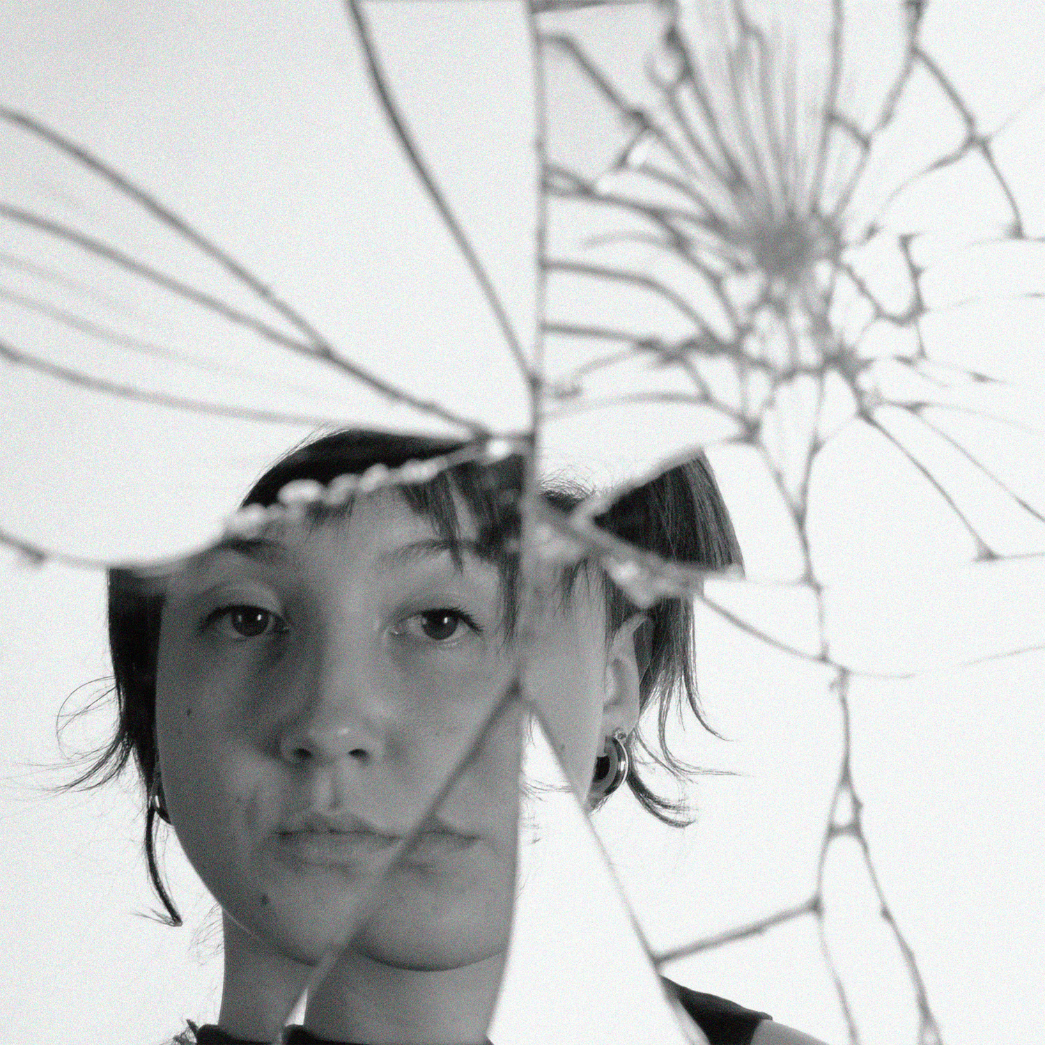 Ritratto in bianco e nero di una persona riflessa su vetro rotto, creando un effetto frammentato e artistico.