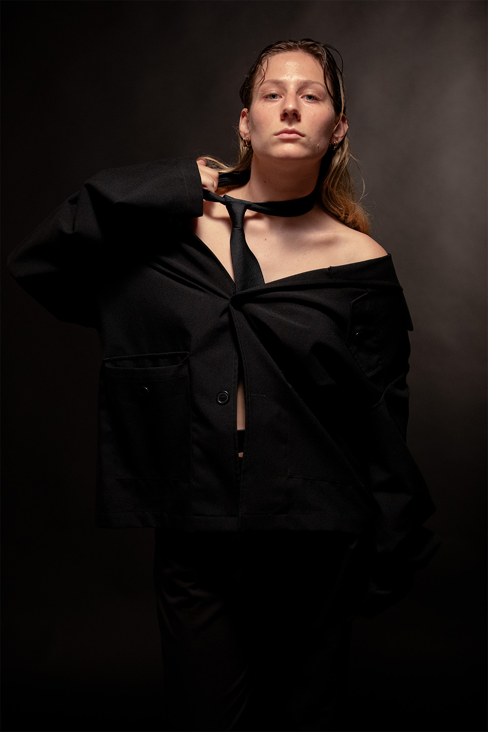 Persona in abito nero e cravatta, posa su sfondo scuro. Mood elegante e deciso.