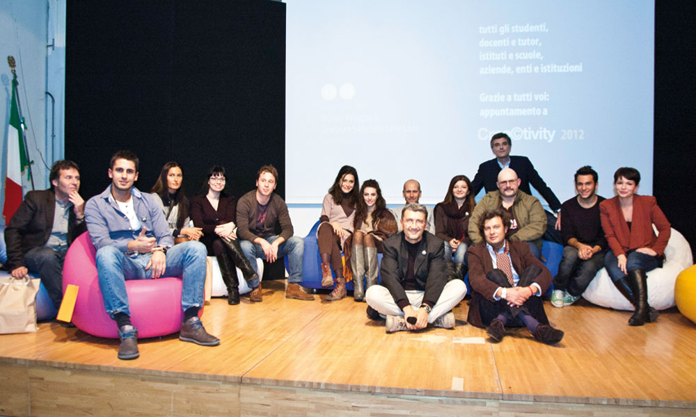 Un gruppo di persone sorridenti sedute su pouf colorati su un palco durante un evento di presentazione.
