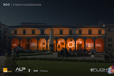 Videoinstallazione notturna su edificio storico illuminato, con pubblico radunato nel cortile di fronte.