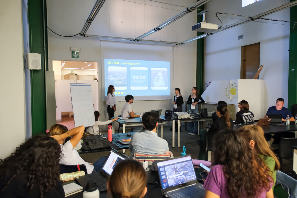 Aula moderna con studenti che ascoltano una presentazione su profili social proiettata su schermo.