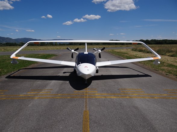 Aereo ultraleggero bianco parcheggiato su una pista asfaltata, con cielo blu e nuvole sullo sfondo.