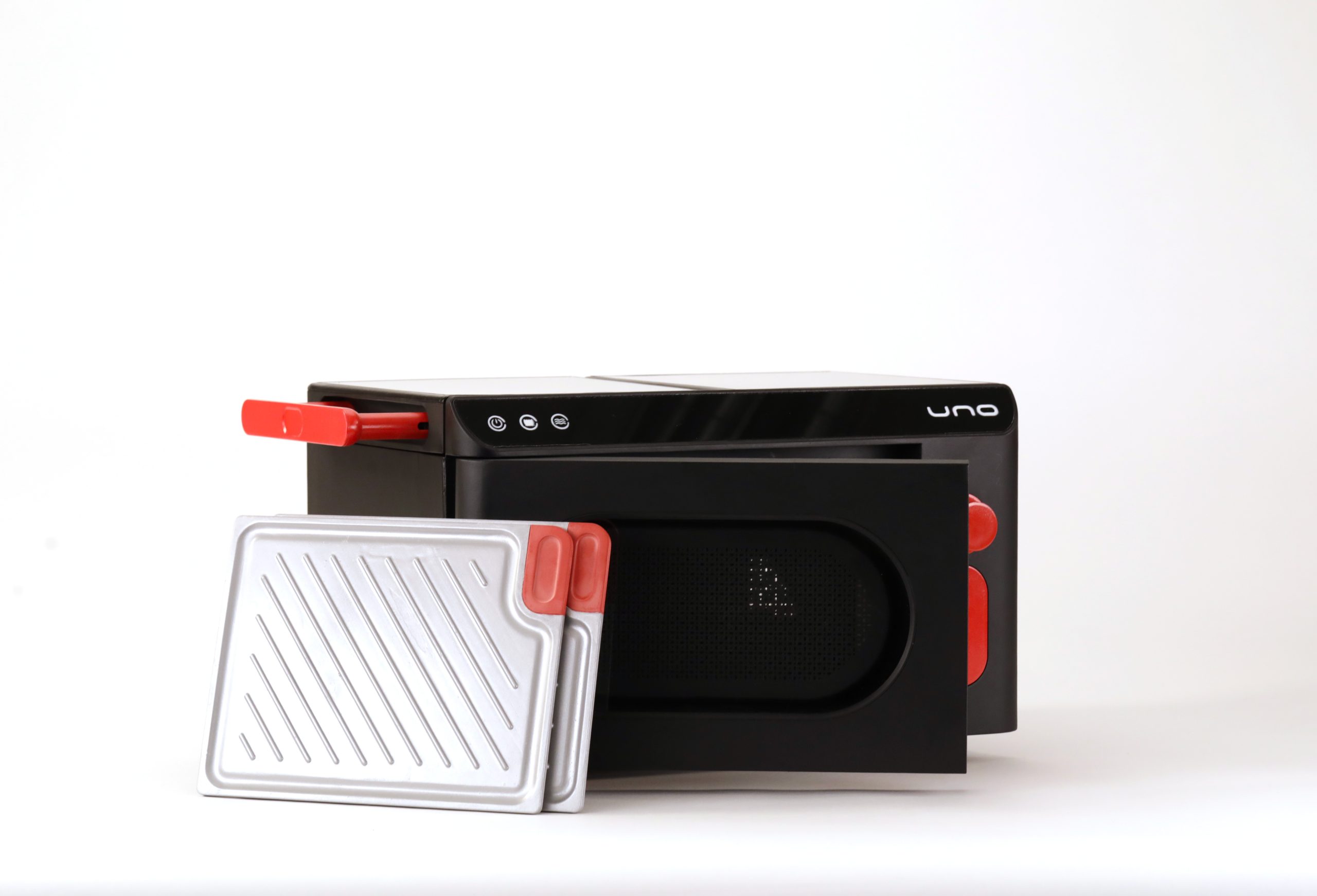 Fornetto da cucina nero con maniglia rossa, accompagnato da due piastre di cottura argentate, su sfondo bianco.