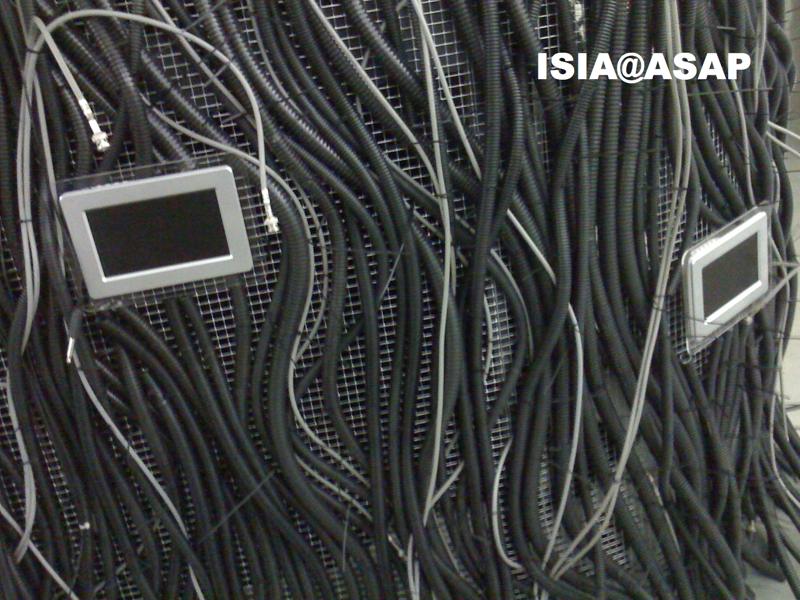 Cavi neri intricati con due schermi su una griglia metallica, sistemi tecnologici complessi.