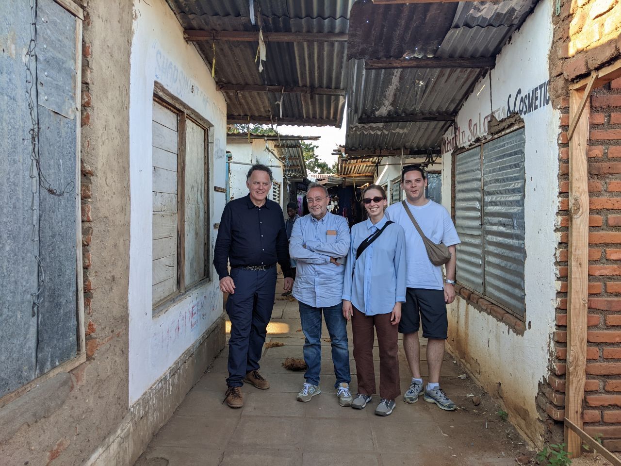 Gruppo di persone in un vicolo con edifici rustici, in una giornata soleggiata.
