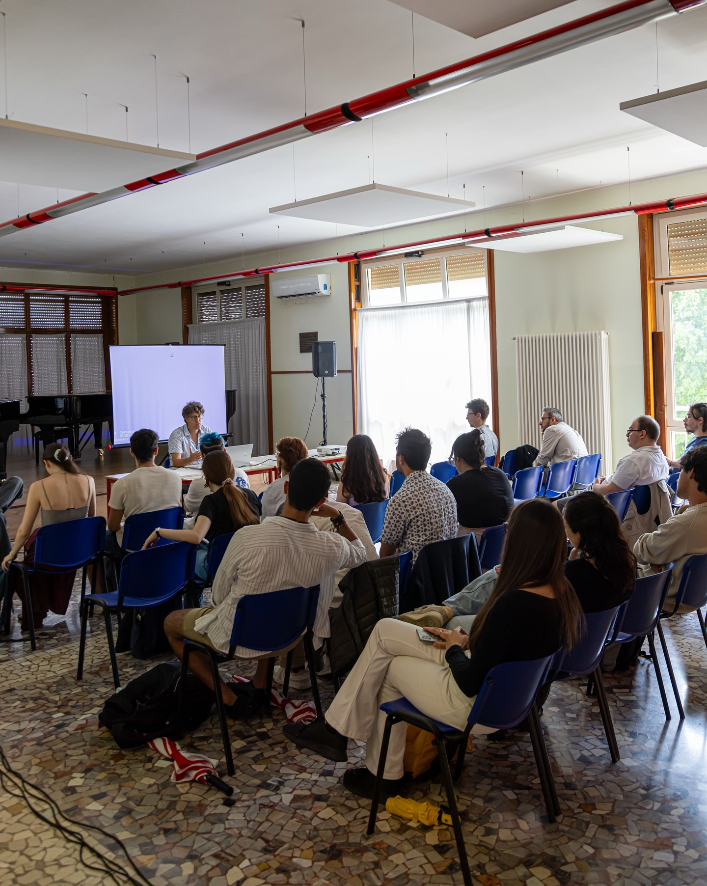 Persone sedute in aula, ascoltano un oratore durante una presentazione con proiettore.