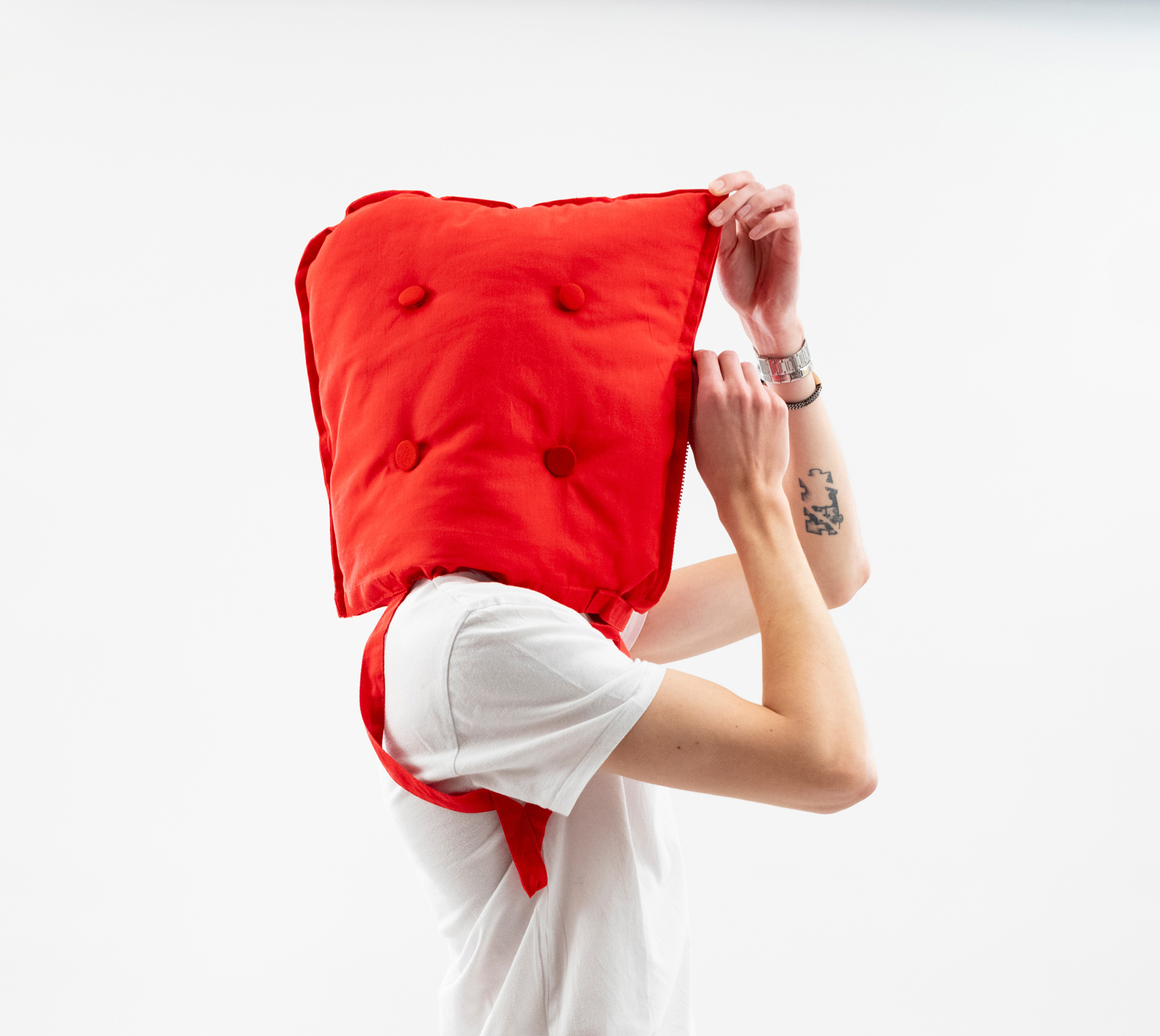 Persona con cuscino rosso in testa, sfondo bianco, indossa t-shirt bianca, concetto creativo e stravagante.
