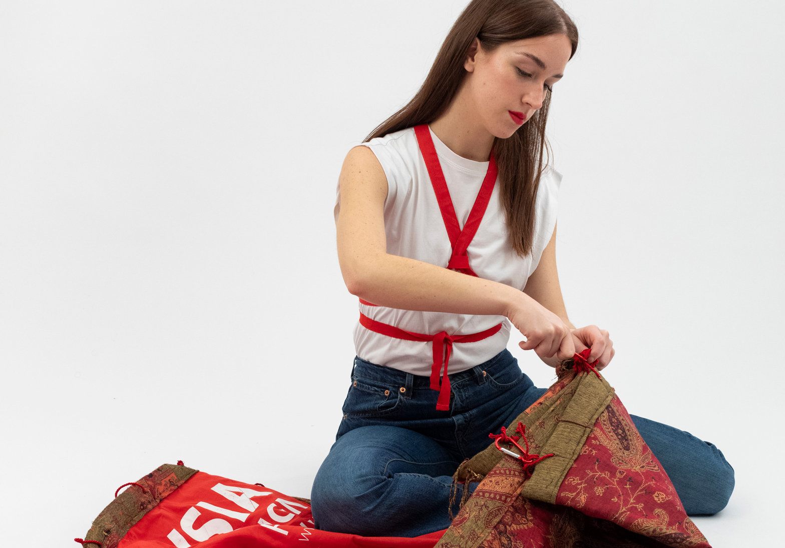 Donna seduta che cuce tessuto decorativo rosso e verde su sfondo bianco.