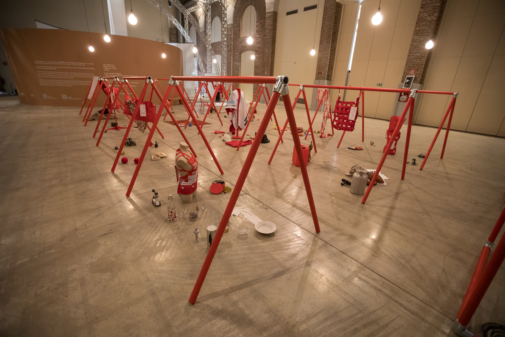 Installazione artistica con strutture rosse e oggetti vari esposti in uno spazio museale luminoso e ampio.