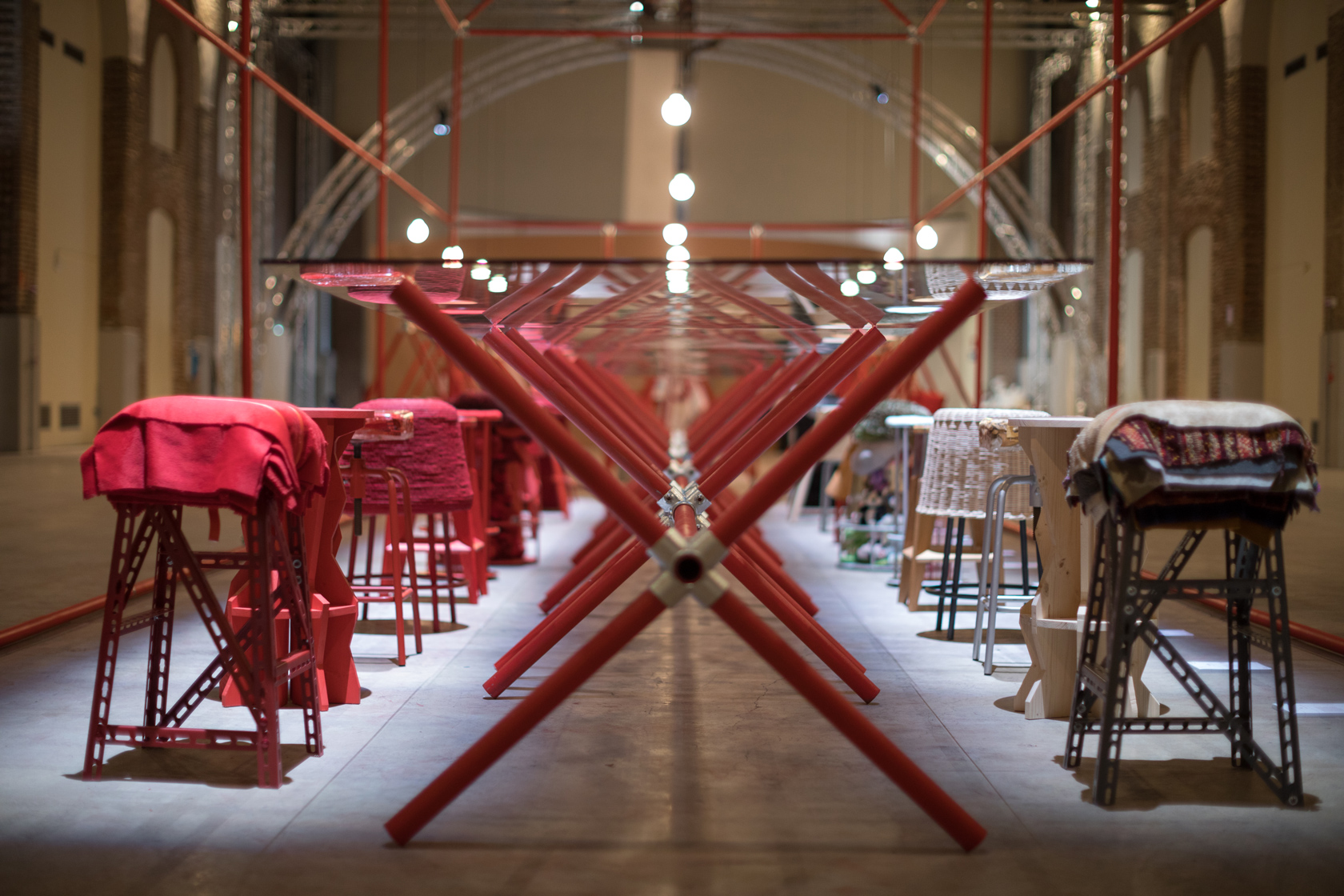 Corridoio con sedie coperte di tessuto colorato e tubi metallici rossi in mostra d'arte moderna.