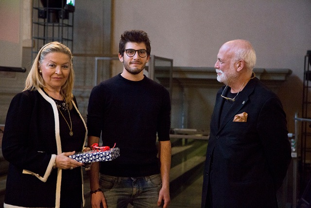 Tre persone in una cerimonia di premiazione, una donna tiene in mano un oggetto incartato.