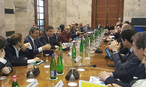 Persone discutono attorno a un lungo tavolo durante una riunione d'affari in una sala conferenze formale.