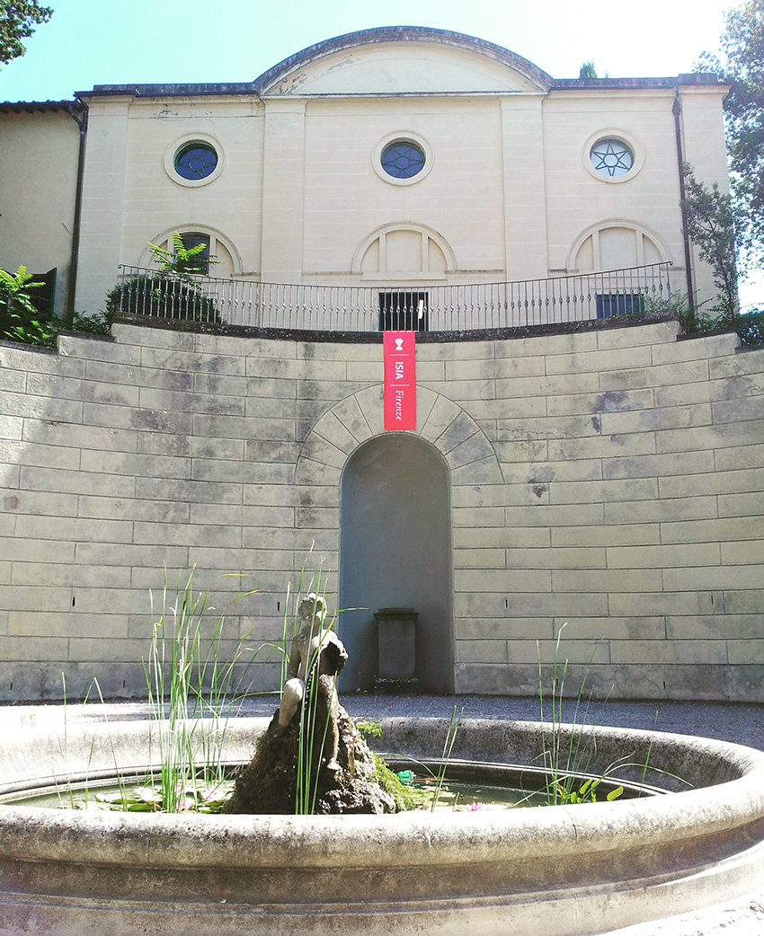 Facciata storica con fontana centrale e piante, edificio antico con dettagli architettonici unici.