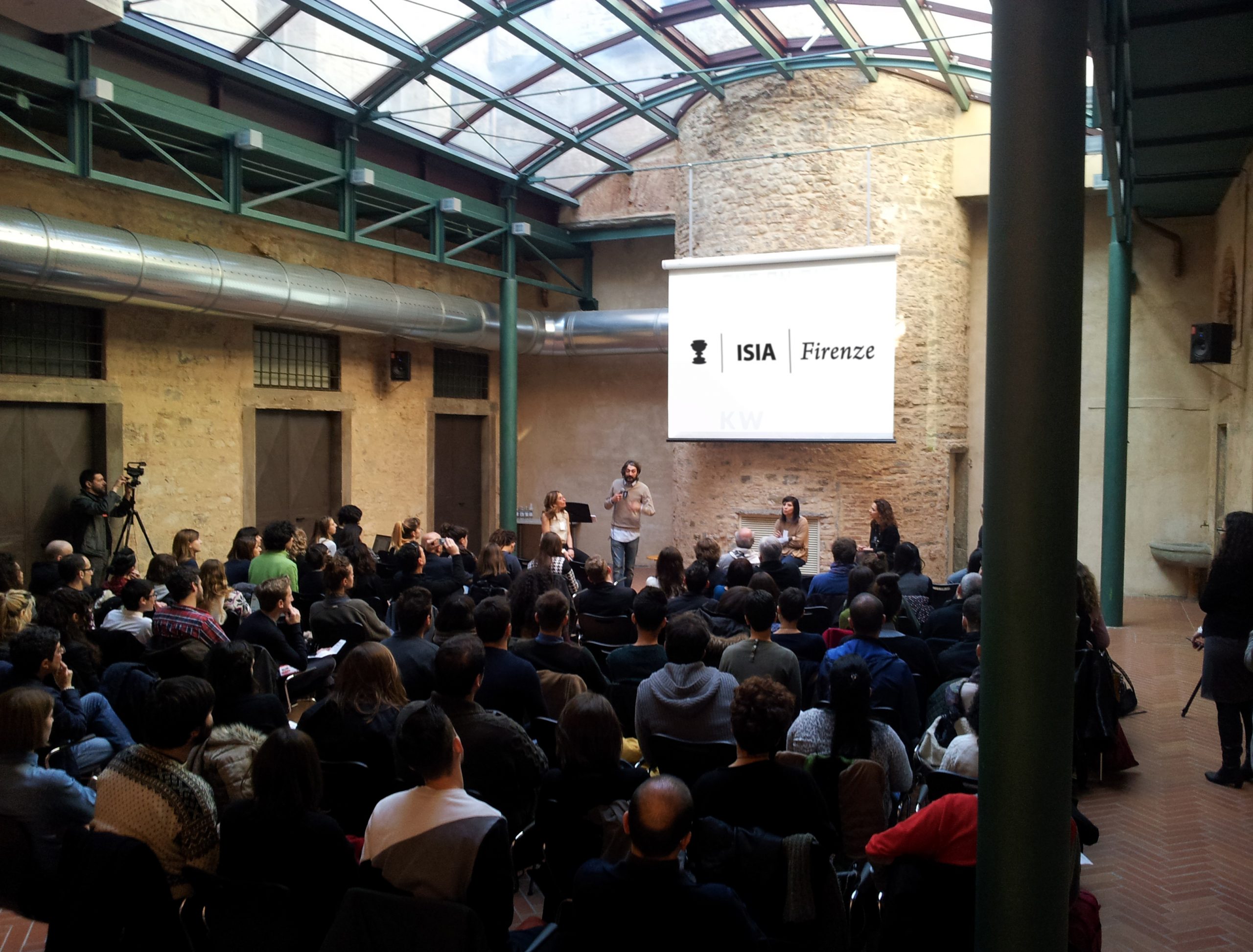 Persone partecipano a un incontro o conferenza presso ISIA Firenze, con un relatore sul palco.