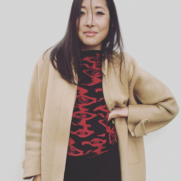 Donna con cappotto beige e maglione rosso a fantasia nera su sfondo bianco.