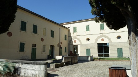 Edificio storico con persiane verdi e cortile alberato sotto il cielo blu.
