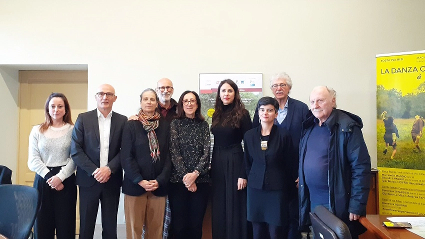 Gruppo di persone in piedi in una sala conferenze con cartellone giallo sulla danza sullo sfondo.