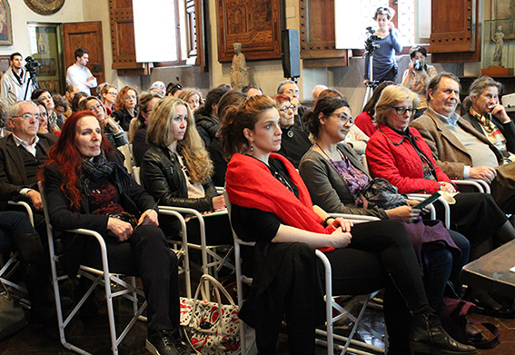 Pubblico attento durante una conferenza in una sala con persone sedute, alcune al lavoro, altre osservano.