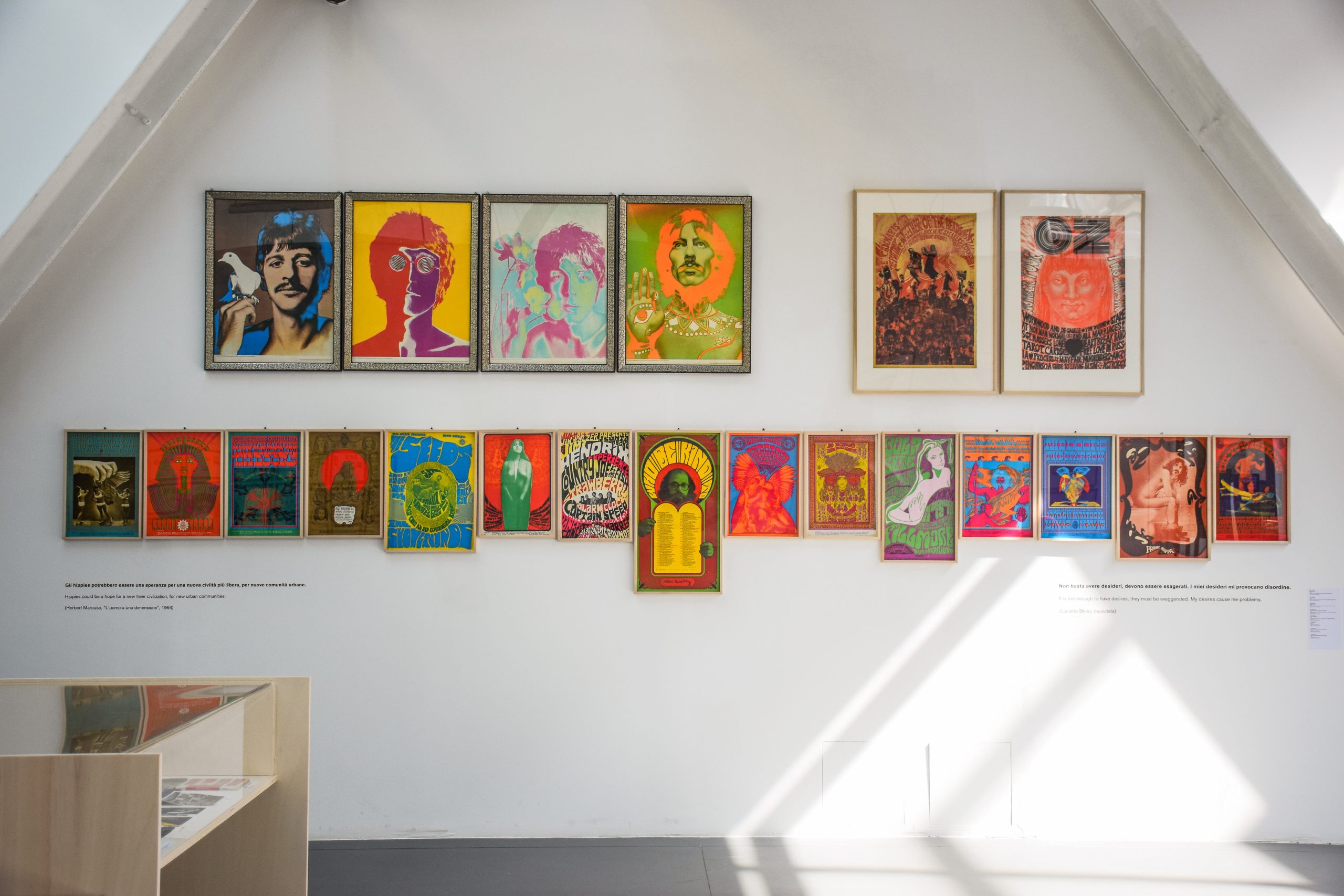 Esposizione di manifesti psichedelici colorati su parete bianca in una mostra d'arte moderna.