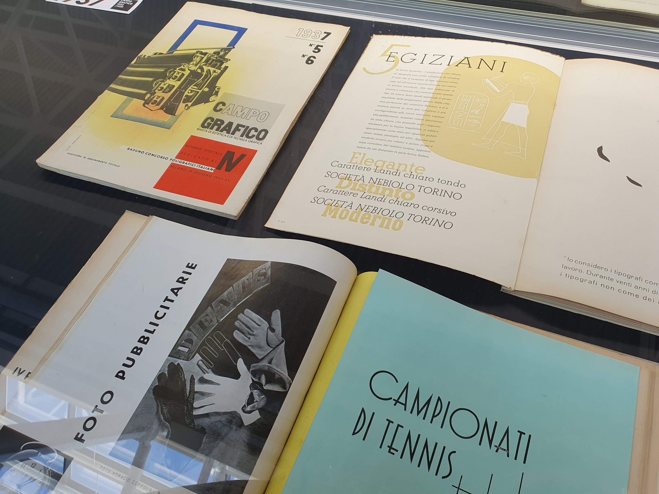 Riviste vintage con design grafico e tipografico in esposizione su una superficie riflettente.