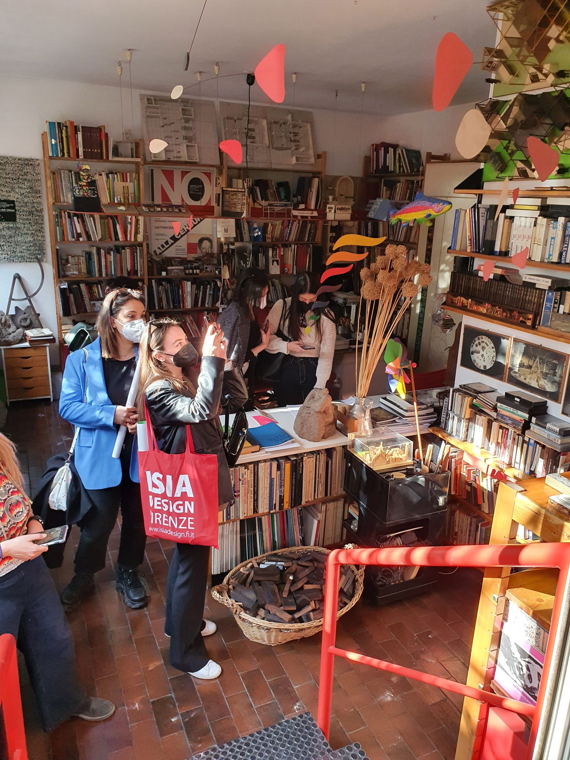 Visitatori in una libreria piena di libri, sculture e oggetti di design, osservano e scattano foto.