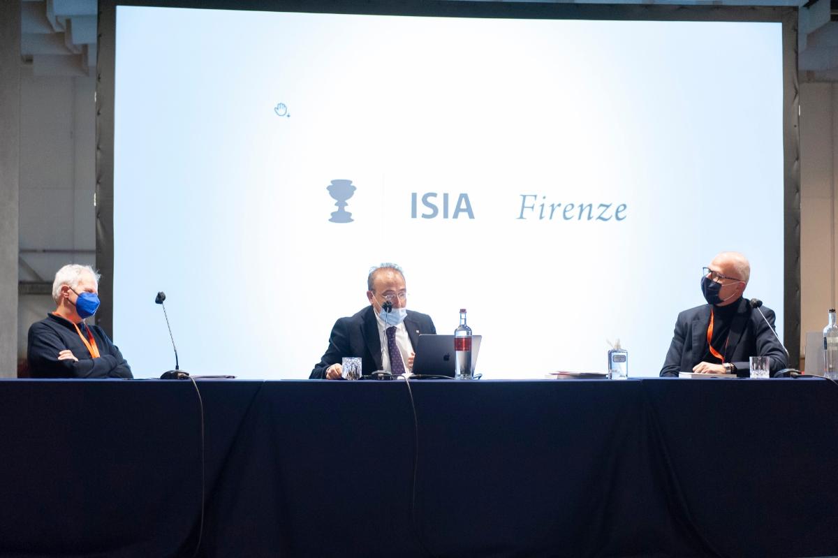 Tre uomini mascherati discutono in conferenza presso ISIA Firenze, seduti a un tavolo con laptop e microfoni.