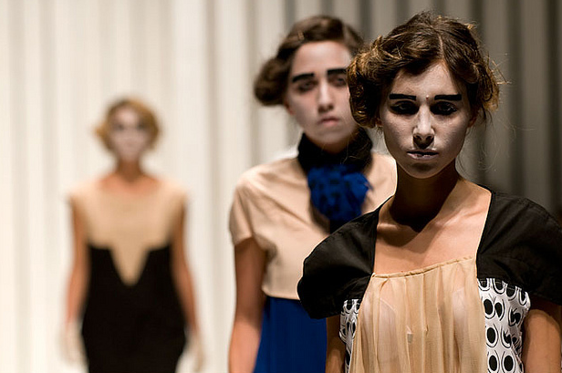 Modelle sfilano in abiti eleganti su passerella, sfondo neutro, moda contemporanea.