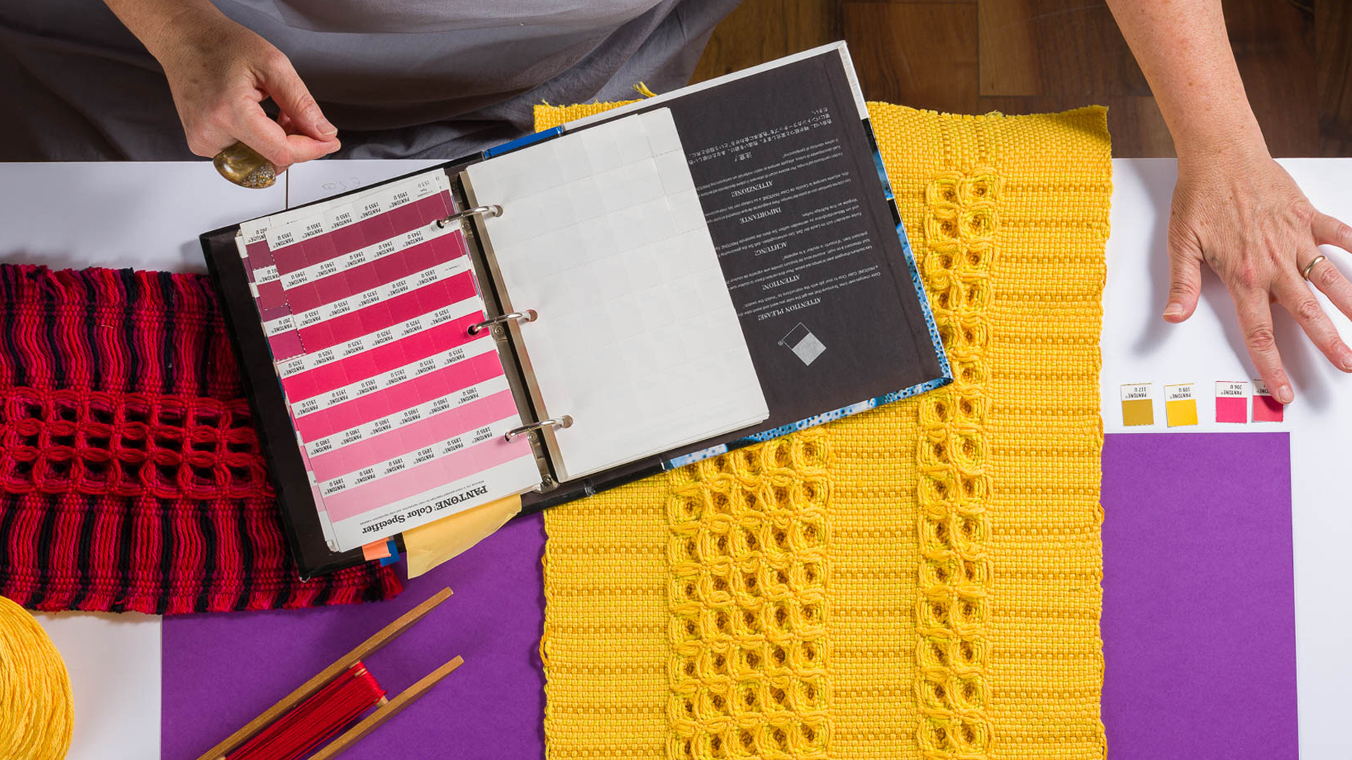 Campioni di tessuto e tabella colori Pantone su un tavolo, evidenziando scelte cromatiche e materiali tessili.