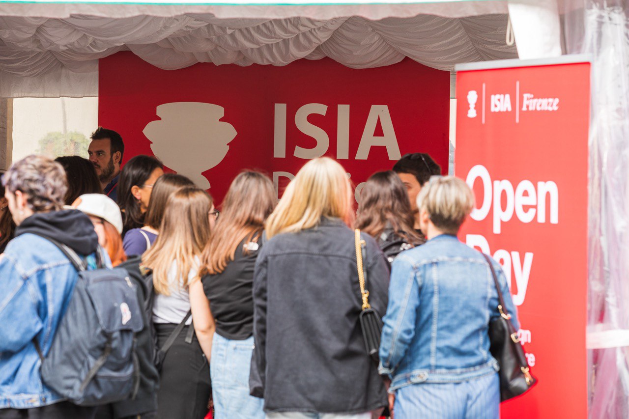 Persone partecipano a un open day presso ISIA Firenze, scambiando informazioni davanti a un banner rosso.