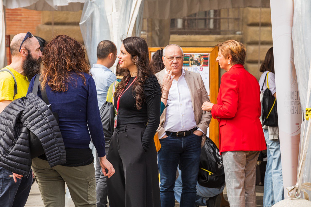 Persone conversano in una fiera all'aperto, indossando abiti casual e professionali, atmosfera vivace.