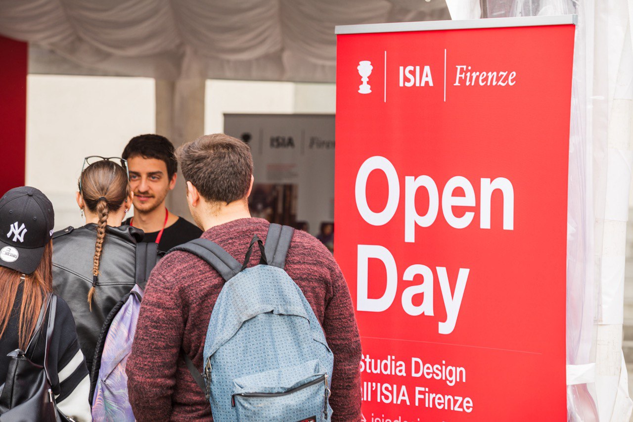 Studenti partecipano all'Open Day dell'ISIA di Firenze, davanti a un cartello rosso informativo sull'evento.