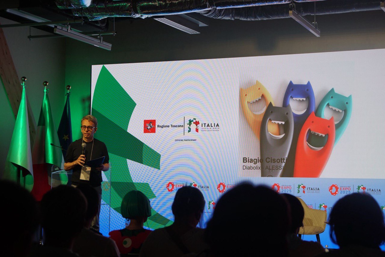 Presentazione all'Expo Italia 2025 con relatore, bandiere italiane e schermo con design di apribottiglie colorati.