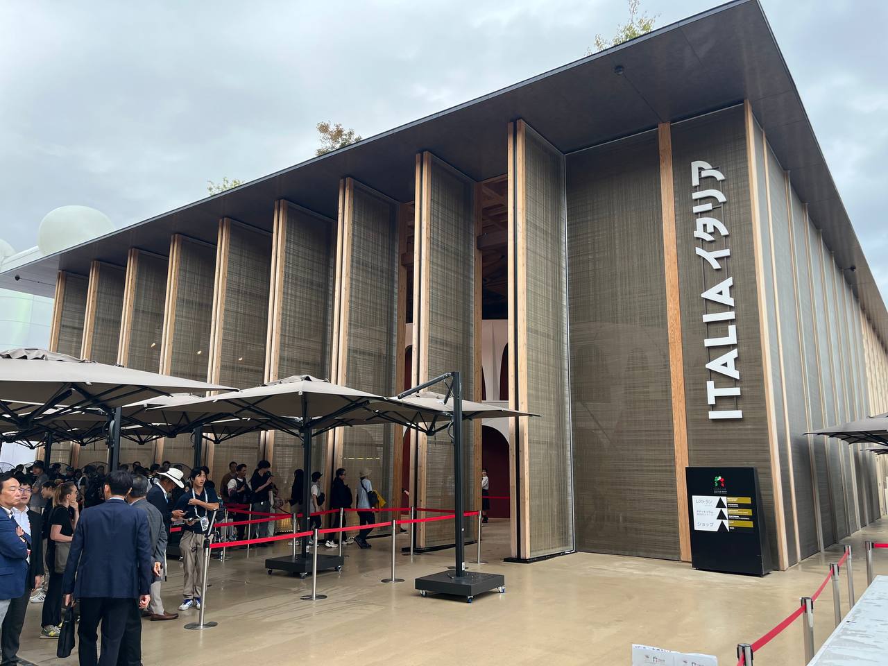 Padiglione Italia con visitatori all'ingresso, struttura moderna e ampie vetrate, cielo nuvoloso sopra.