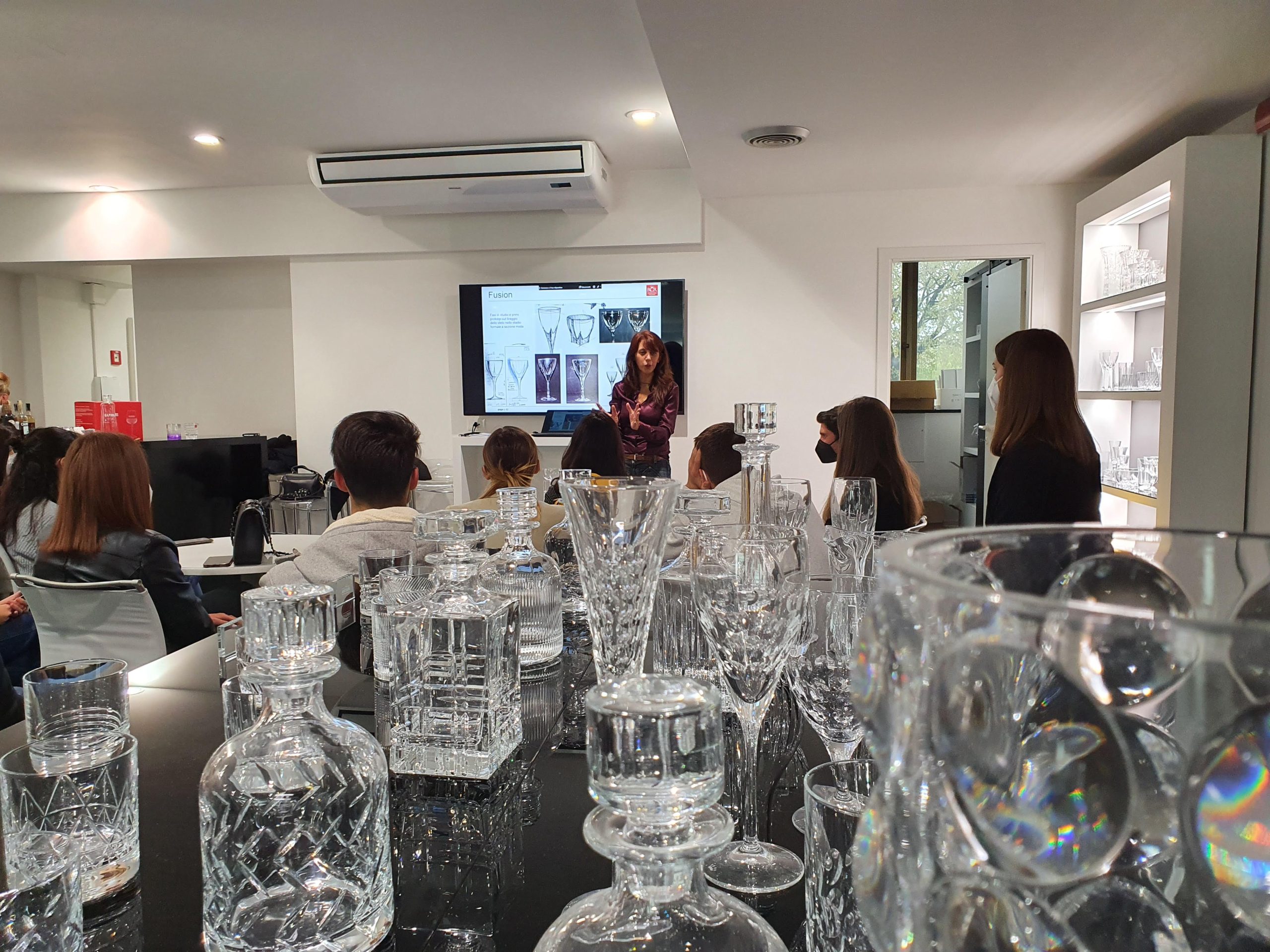 Lezione su bicchieri di cristallo con presentazione in aula, partecipanti seduti e attenti.