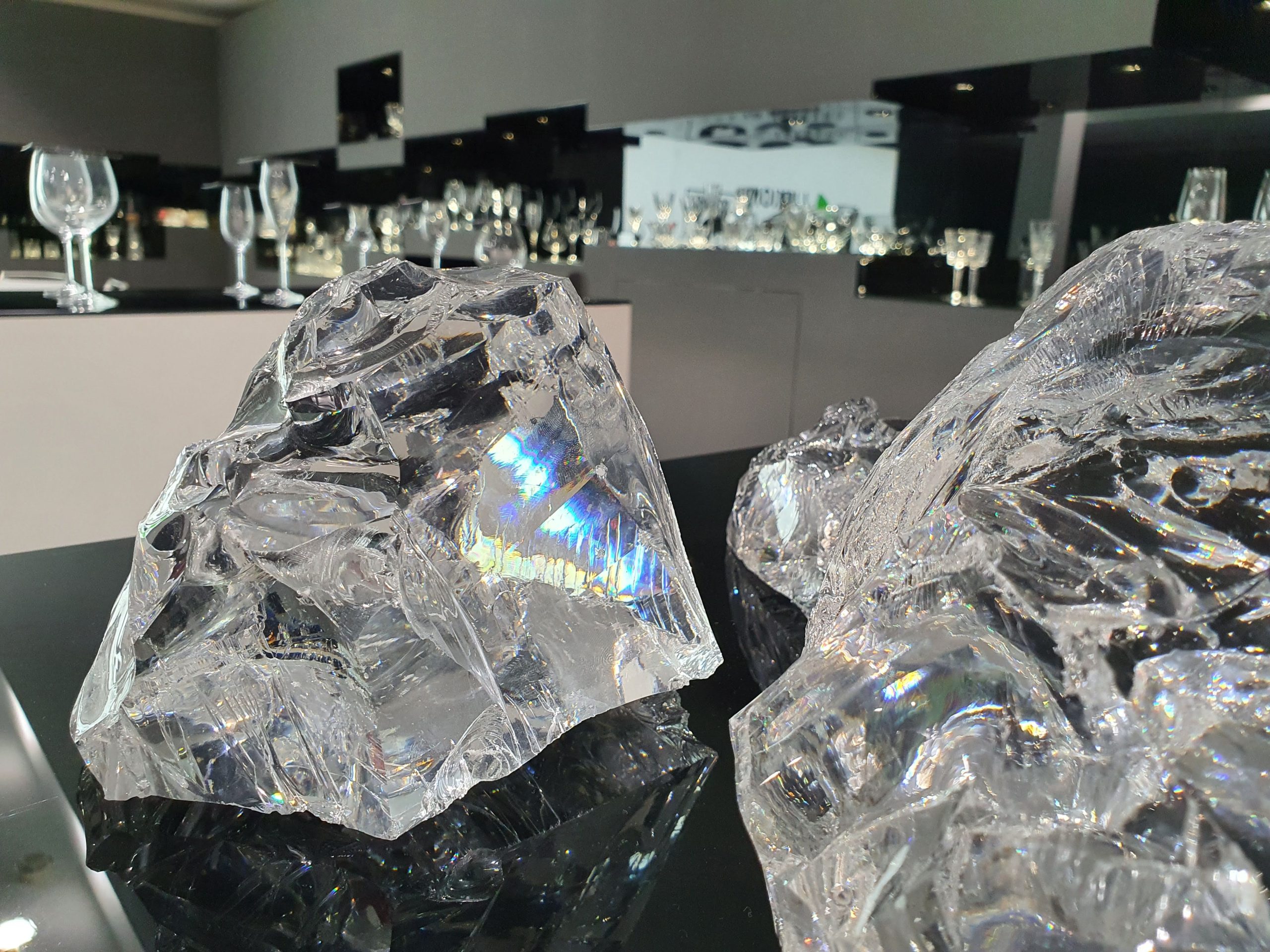 Cristalli di ghiaccio riflettono la luce su un tavolo elegante, con bicchieri di vetro sullo sfondo.