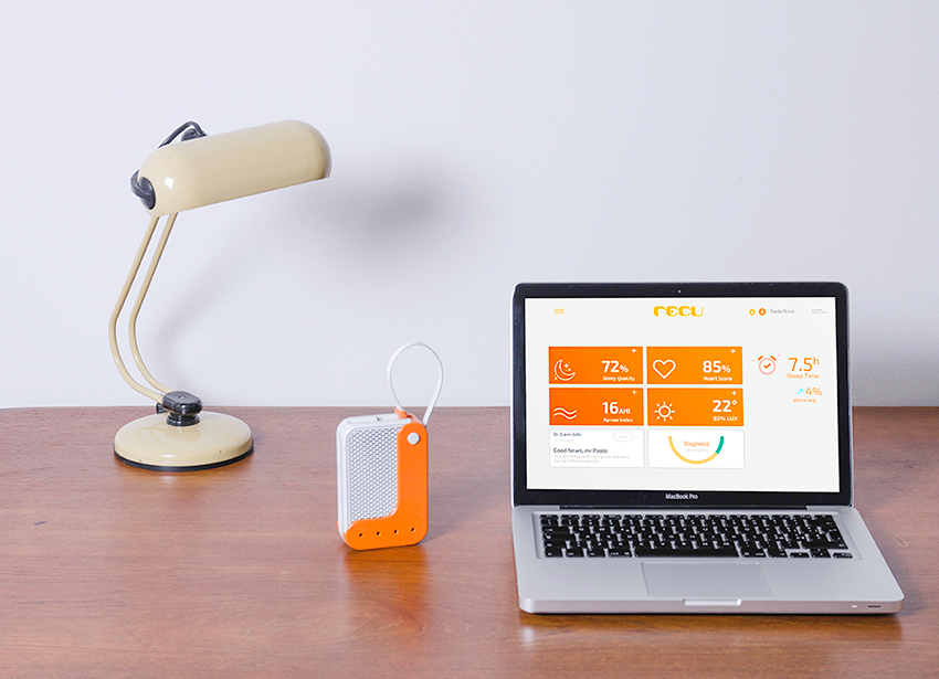 Laptop con app di monitoraggio del sonno su scrivania di legno, affiancato da lampada e dispositivo portatile arancione.