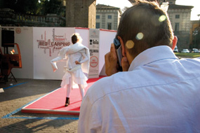 Fotografo scatta foto a modello su passerella con abito bianco durante evento all'aperto su tappeto rosso.