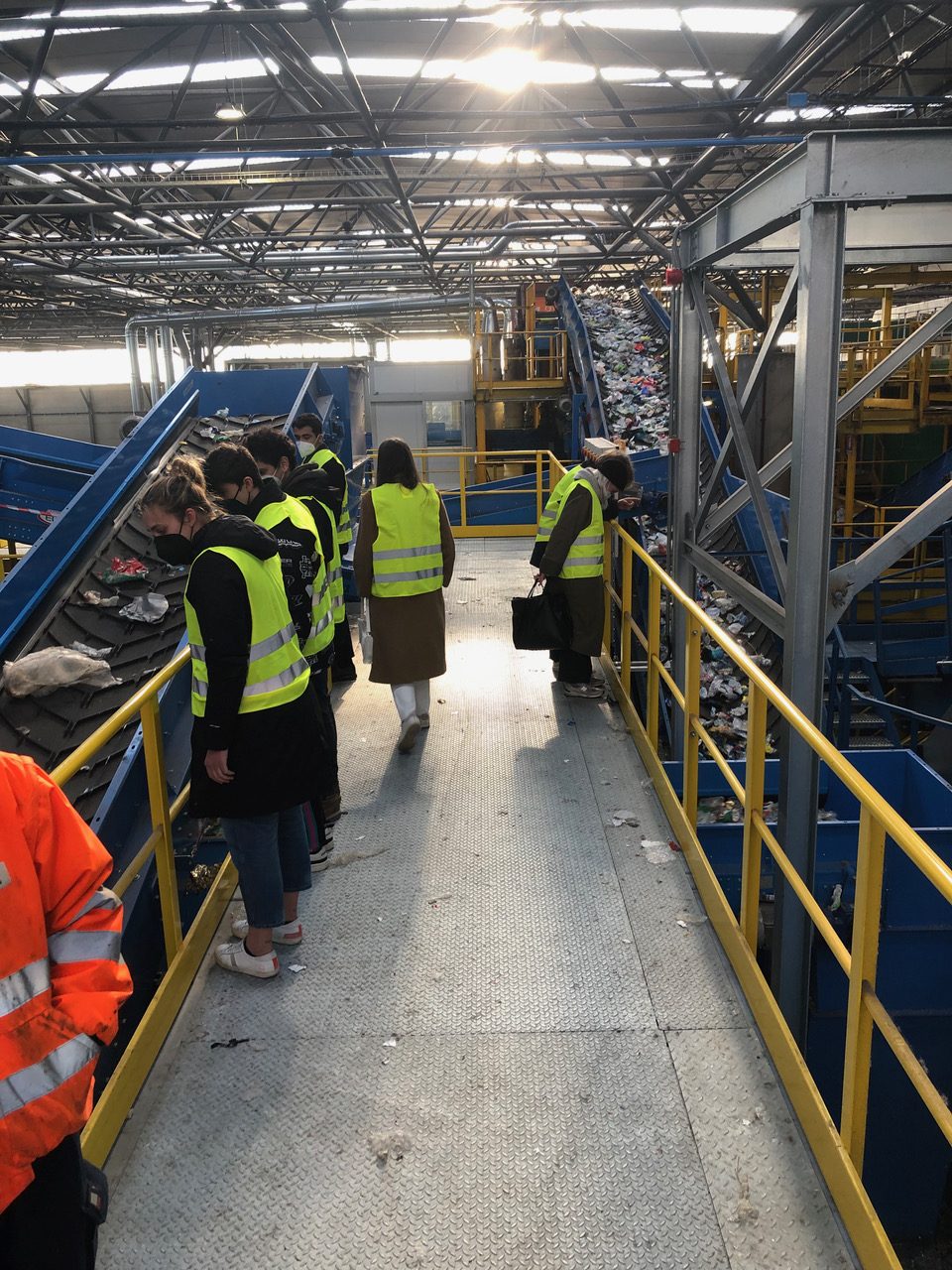Personale in giubbotti gialli osserva processo di smistamento rifiuti in un impianto di riciclaggio.