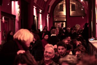 Folla in un locale affollato con luci soffuse e atmosfera vivace, persone conversano e si godono la serata.